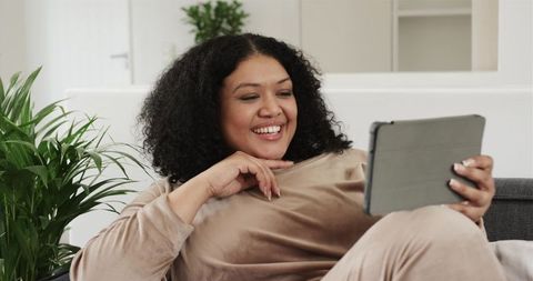 Smiling African American Woman Reclining on Sofa Holding Tablet in Cozy Living Room Daytime