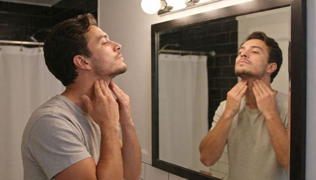 Young man checking jawline and neck in bathroom mirror during morning grooming routine