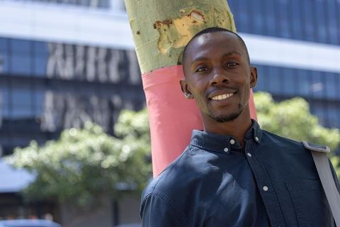 Smiling african professional leaning on pink-wrapped tree in modern city street