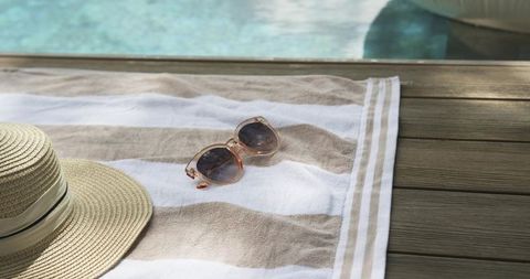 Relaxing poolside moment with striped towel, straw hat and sunglasses