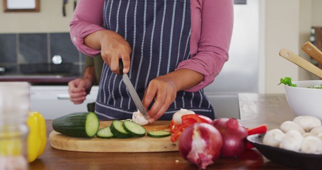 Person slicing various vegetables including cucumbers, tomatoes, and onions on a cutting board in a kitchen. Perfect for culinary blogs, healthy eating promotions, cooking tutorials, and kitchen equipment advertisements.