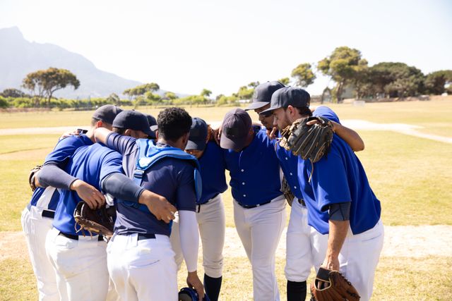 Multi ethnic team of male baseball players before a game in baseball field on a sunny day, forming a huddle interacting motivating each other. Baseball sports competition.