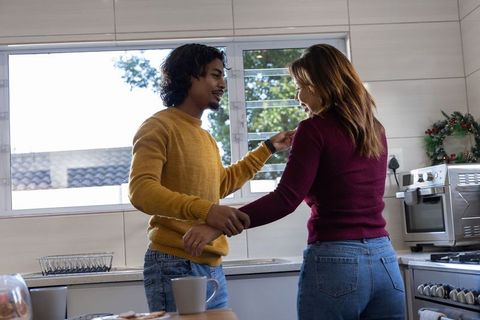 Young couple sharing cozy morning in sunlit kitchen holding mugs and laughing