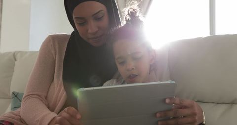 Mother and daughter using tablet together on cozy sofa