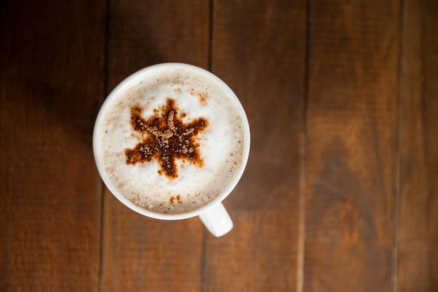 Top-down view of a cup of coffee with intricate star-shaped latte art on a wooden table. Perfect for use in coffee shop promotions, breakfast menus, blogs, social media posts, and websites related to coffee culture and beverages.
