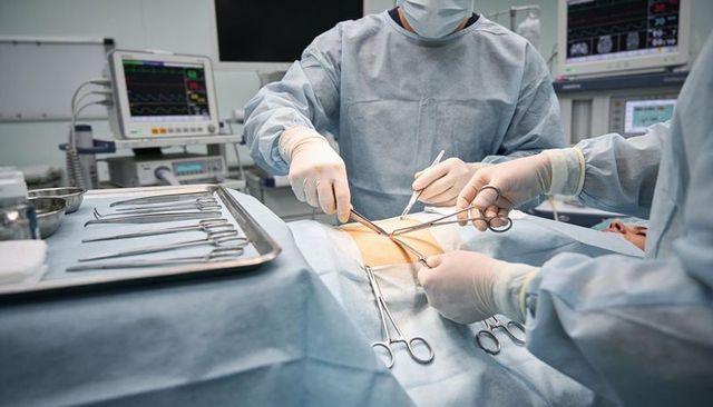 Surgical team performing abdominal operation with sterile instruments and patient monitors