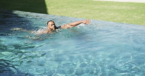 Mature male swimming laps in backyard pool reaching toward edge under sunny shadow