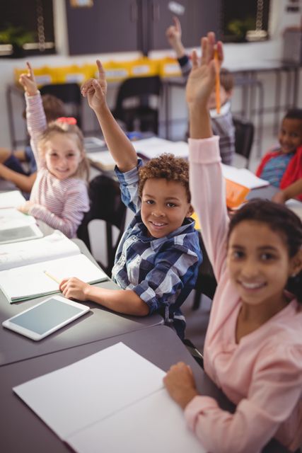 Portrait of happy schoolkids raising their hands in classroom at school