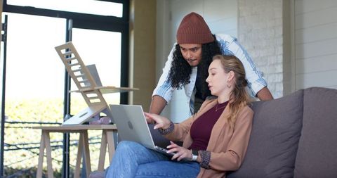 Diverse coworkers collaborating on laptop in modern home office lounge near glass doors