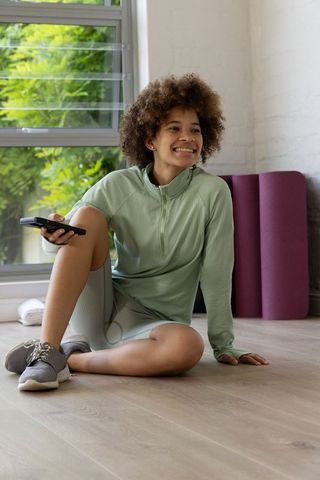 African american woman relaxing after home workout holding remote by window with yoga mats