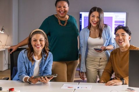 Multicultural team collaborating around desk with tablet, laptop and monitor in modern office
