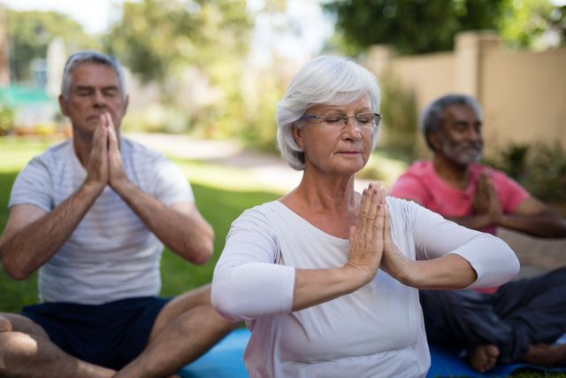 Senior people with closed eyes meditating while sitting in prayer position at park