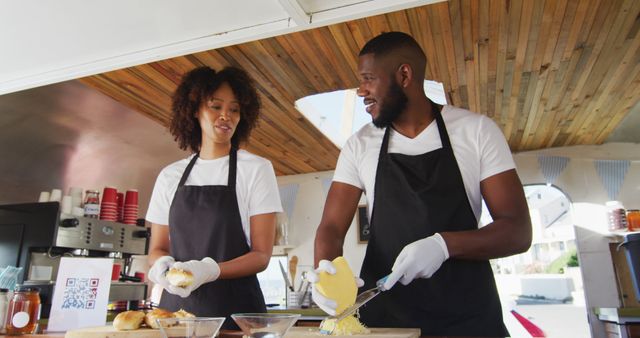 African american couple wearing aprons smiling while preparing hot dogs together in the food truck. food truck and street food concept