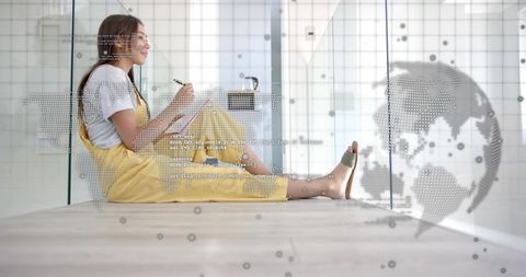 Woman sitting on floor writing in notebook with dotted world map overlay, modern coworking