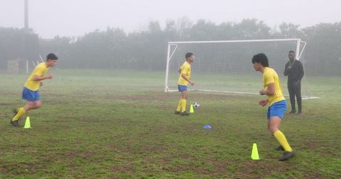 Soccer Team Training on Misty Field with Coach Conducting Drills