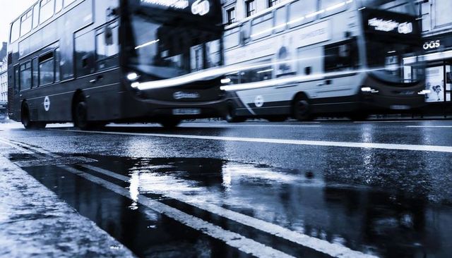 Rainy city street with motion blur double-decker buses and puddle reflections