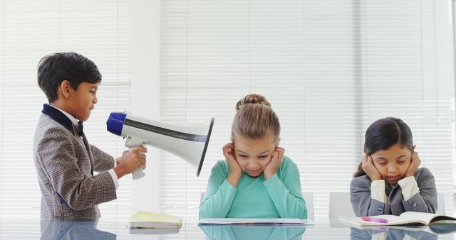 Boy using megaphone near two annoyed classmates covering ears. Bright classroom scene ideal for representing disruptive behavior, school conflicts, or communication issues among children. Useful for blogs, educational articles, and social media posts discussing classroom dynamics or problem behaviors.