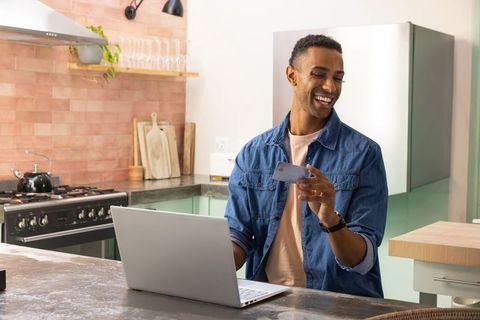 Smiling african american man working remotely at kitchen counter with laptop and phone