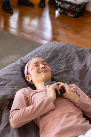 Relaxed woman with gel eye patches holding smartphone