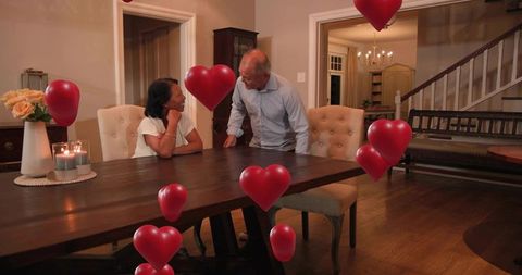 Senior couple enjoying romantic dinner at home with heart balloons and cozy candlelight