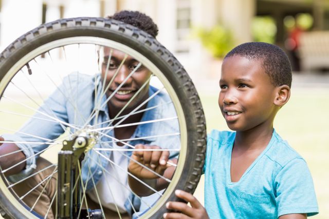 Father and son are repairing a bicycle together outdoors. The father is guiding his son, who is smiling and engaged in the activity. This image can be used to illustrate family bonding, teamwork, parenting, and outdoor activities. It is ideal for use in advertisements, educational materials, and articles about family life, childhood, and learning new skills.