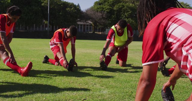 A group of young soccer players stretching on a green field, wearing red uniforms. They are preparing for a game or a training session. The image captures the spirit of teamwork and the importance of physical fitness in sports. Suitable for use in articles about sports training, teamwork, youth athletics, or fitness routines.
