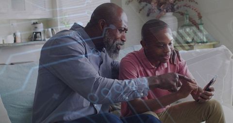 Black father guiding teen son on smartphone with augmented reality, mentoring and bonding at home
