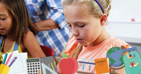 Blonde girl focusing at classroom desk with colorful school supplies and teacher nearby