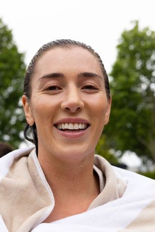 Smiling woman posing outdoors wrapped in beige-and-white towel after swim
