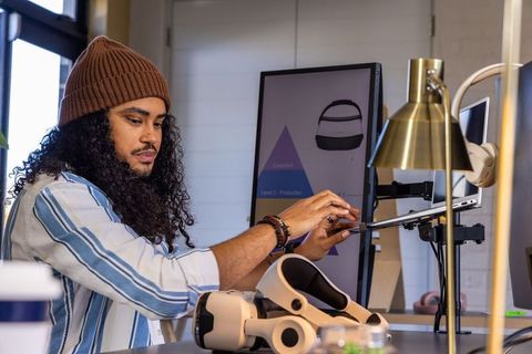 Vr designer adjusting tablet on articulating arm at workspace with headset and controllers