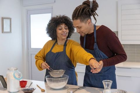 African american couple baking together, sifting flour in sunlit modern kitchen