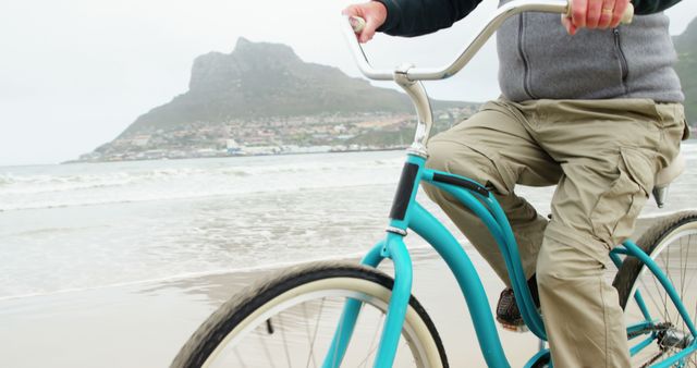 A middle-aged Caucasian man rides a bicycle along a scenic beach, with copy space - Download Free Stock Photos Pikwizard.com