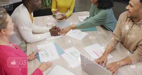 Diverse team collaborating at table reviewing charts and exchanging handshake