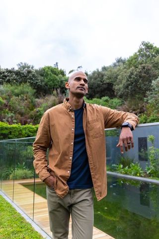 Asian man leaning on glass railing by backyard pool terrace wearing smartwatch