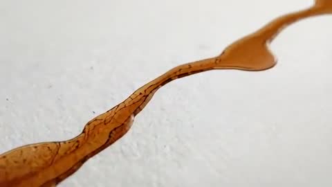 Macro video showing brown viscous pigment flowing across textured paper forming rivulet and bubbles
