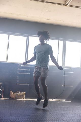Man skipping rope in sunlit gym studio showing fitness, energy and determination, strength