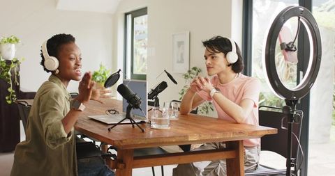 Diverse co-hosts recording podcast in bright home studio with microphones and laptop