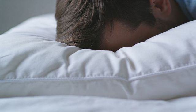 Man pressing face into white pillow, resting quietly, cozy bedroom closeup texture