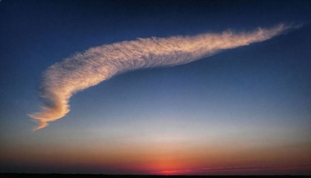 Sunlit curved cloud arching over colorful sunset horizon with rippled texture