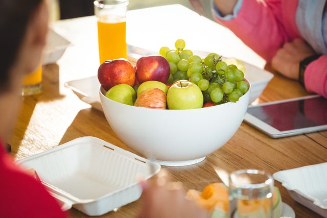 Bowl of fresh fruits including apples and grapes on a wooden table in an office setting. Ideal for promoting healthy eating habits at work, wellness programs, office break times, and team meetings. Can be used in articles about workplace wellness, healthy snacks, and office culture.