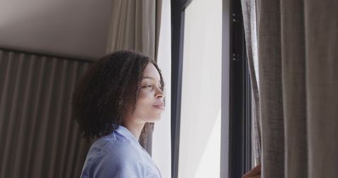 African american woman standing by hotel window parting curtains and contemplating view