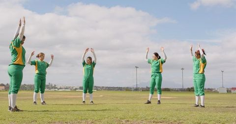 Female athletes stretching on sports field in green and yellow uniforms
