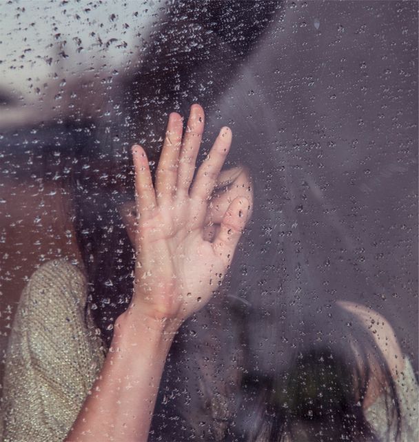 Woman's hand against a window with raindrops, portraying a sense of solitude and melancholy. Useful for themes involving emotions, loneliness, and reflective moods. Could be utilized in websites, blog posts, or articles about mental health, rainy day introspection, or emotions.