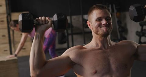 Athletic man performing dumbbell shoulder press at gym