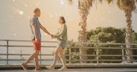 Happy couple holding hands by sea in sunlight