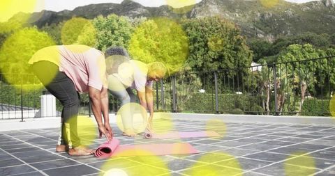 Seniors unrolling pink yoga mats on rooftop terrace exercising together with mountain view
