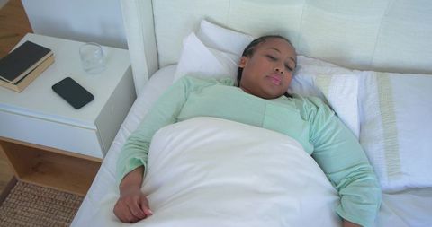 Mid adult african american woman sleeping peacefully in bed with smartphone nearby