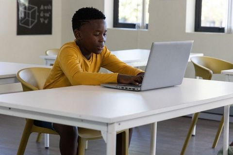 African american teen typing on laptop in bright classroom studying stem and coding