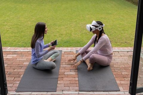 Women practicing outdoor yoga while using virtual reality headset and tablet