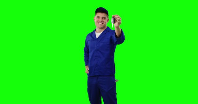 Smiling mechanic in blue overalls holding tool against green background - Download Free Stock Images Pikwizard.com